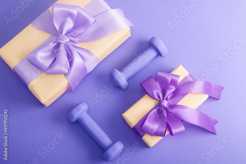Holiday birthday party sport flat lay composition with purple dumbbells and craft gifts with lilac bow on  violet paper background. Top view  horizontal orientation