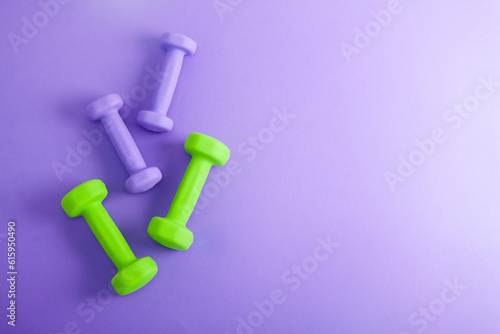 Sport flat lay composition with purple and green dumbbells on violet concrete background. Top view,  horizontal orientation