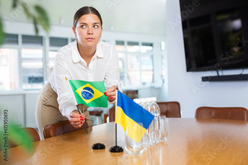 Assistant girl prepares office for international negotiations and meetings of leaders. Lady sets miniatures flags of Ukraine and Brazil on table. Close-up