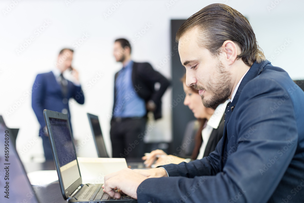Workplace in modern corporate office with business people brainstorming. Businessman working on laptop during the meeting. Workplace in modern corporate office with business people brainstorming. Businessman working on laptop during the meeting.