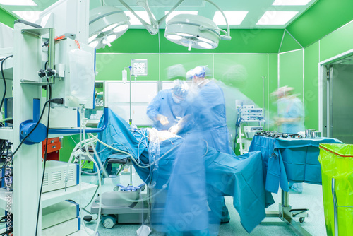 Team of doctors, motion blurred figures, are performing surgery in modern hospital.
