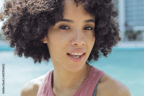 Headshot of pretty black girl with short curls and in casual outfit looking sensually at camera on city riverbank.