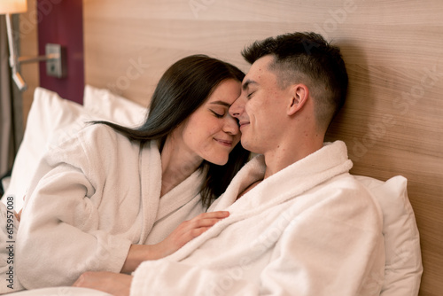 portrait young couple on honeymoon in hotel room lying on bed in white robes kissing happy lovers travel concept