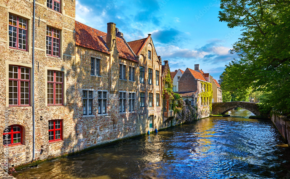 Fototapeta premium Bruges Belgium vintage stone houses and bridge over canal ancient medieval street picturesque landscape in summery sunny day with blue sky white clouds.