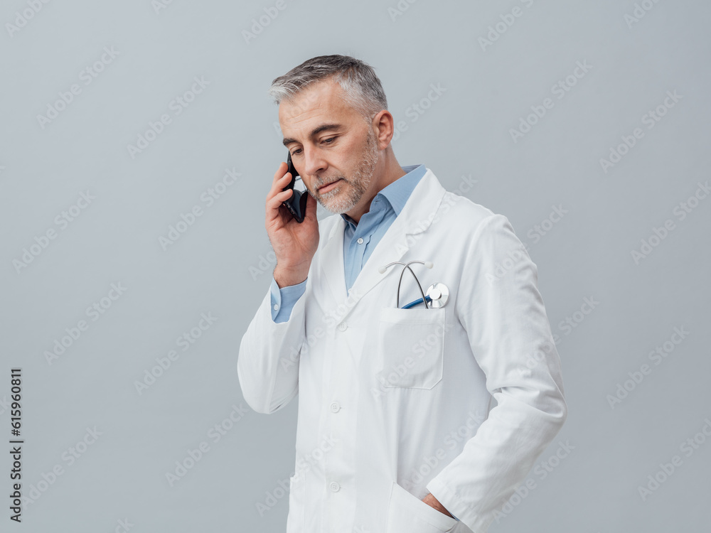 Confident mature doctor having a phone call with his smartphone: medical service consultation by phone Confident mature doctor having a phone call with his smartphone: medical service consultation by phone