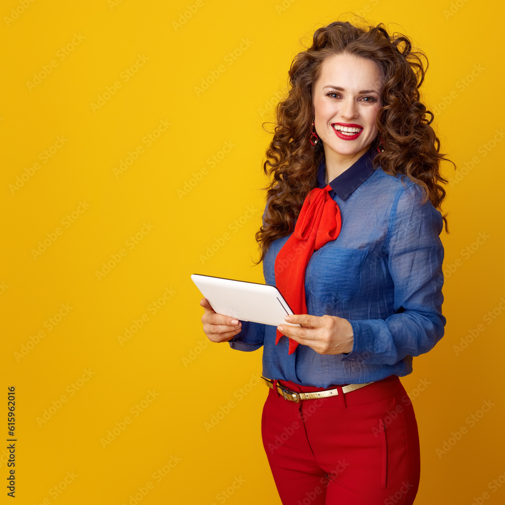 smiling trendy woman with long wavy brunette hair with tablet PC on yellow background smiling trendy woman with long wavy brunette hair with tablet PC on yellow background