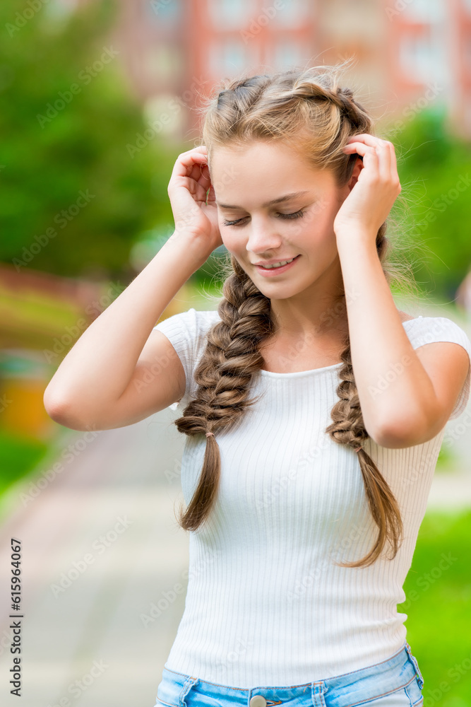 beautiful girl with two braids corrects hands hair, close-up portrait in the park
