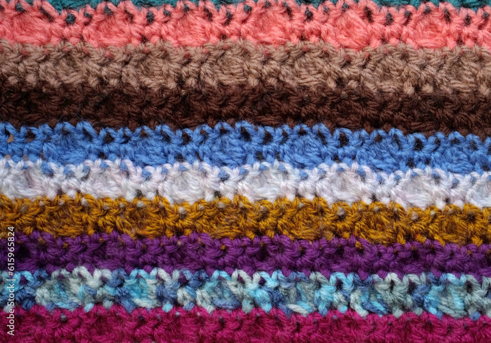 Background of crocheted stitches in multi-coloured stripes, soft yarn texture