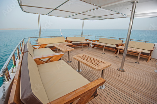 Rear teak deck of a large luxury motor yacht with chairs sofa table and tropical sea view background © Designpics