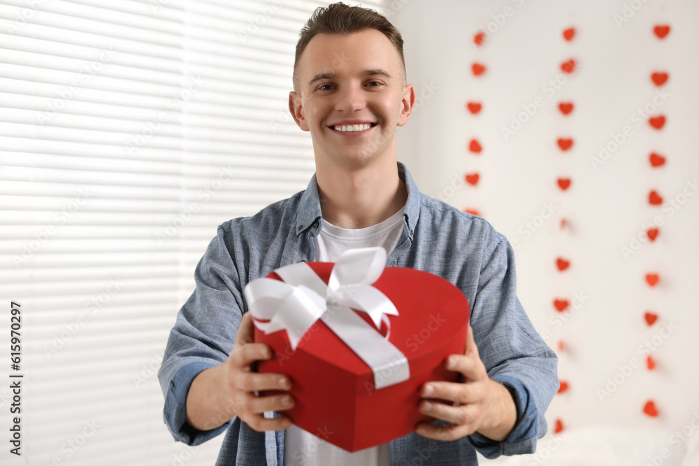 Handsome young man with gift box indoors, view from camera. Valentine's day celebration in long distance relationship Handsome young man with gift box indoors, view from camera. Valentine's day celebration in long distance relationship