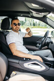 vertical photo of a young man in glasses driving a luxury car posing at the camera