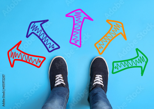 Choosing future profession. Teenager standing in front of drawn signs on light blue background, top view. Arrows pointing in different directions symbolizing diversity of opportunities