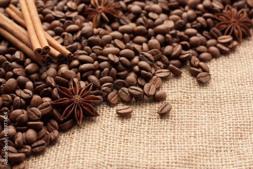 Roasted coffee beans are scattered on sackcloth with star anise and cinnamon sticks. There is copyspace for your text.