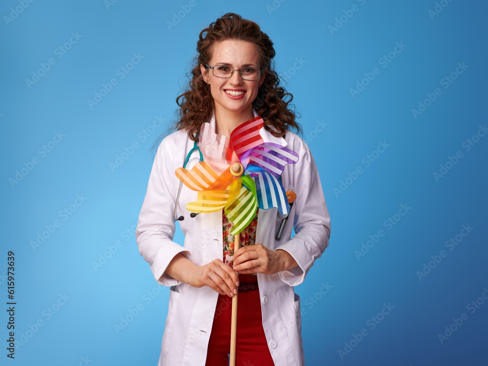 happy pediatrist doctor in white medical robe with colorful windmill isolated on blue background happy pediatrist doctor in white medical robe with colorful windmill isolated on blue background