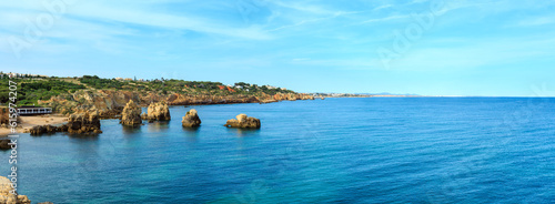 Summer Atlantic coast landscape with rock formations near shore and beach Praia dos Arrifes or Praia dos Tres Penecos, Albufeira, Algarve, Portugal. Two shots stitch panorama. People unrecognizable.