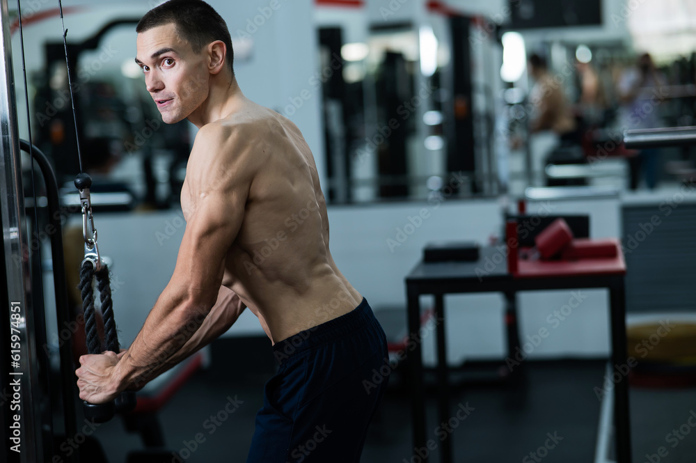 Shirtless man doing triceps pulldown at the gym. 