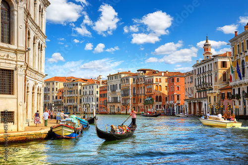 Venice, Italy. Gondolas with tourists floating by Grand Canal among antique buildings and traditional italian Venetian architecture. Sunny day with blue sky and clouds.