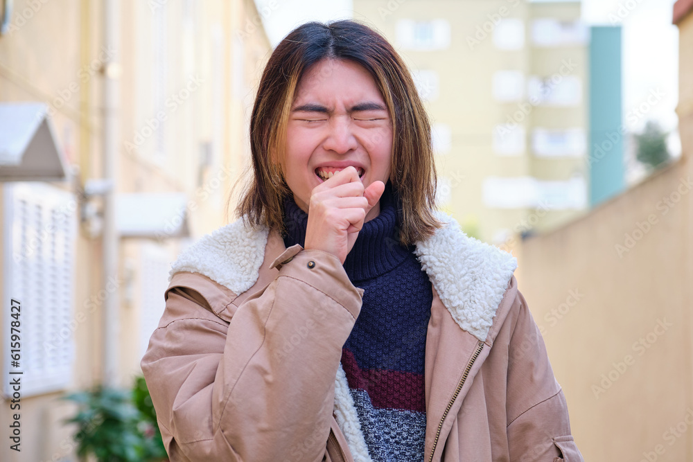 Fototapeta premium Young taiwanese man sneezing outdoor in winter. Fever, flu, illness concepts.