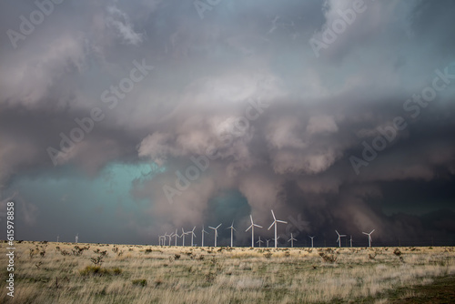 Wind turbines spin as a huge storm with a dark, low wall cloud approaches.