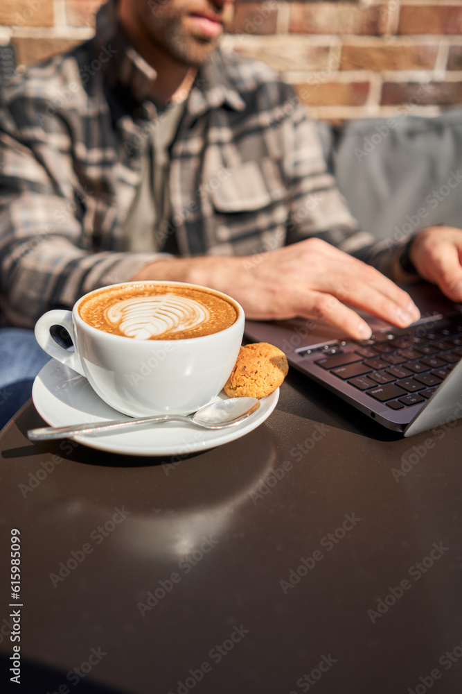 Portrait of a handsome successful smart man drinking coffee and looking at a laptop. A business man is having breakfast sitting on a beautiful terrace in a cafe. Reading, browsing the Internet Portrait of a handsome successful smart man drinking coffee and looking at a laptop. A business man is having breakfast sitting on a beautiful terrace in a cafe. Reading, browsing the Internet