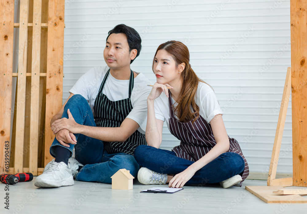 Asian professional male and female carpenter worker lover couple colleague in apron sitting on floor discussing talking writing information data short notes on clipboard in home decoration workshop Asian professional male and female carpenter worker lover couple colleague in apron sitting on floor discussing talking writing information data short notes on clipboard in home decoration workshop