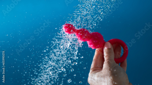 Fotografija Woman holding pink anal beads under running water on blue background