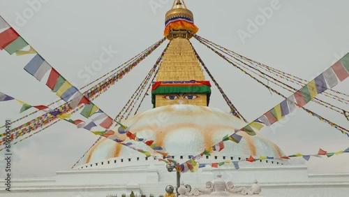 Panning down clip of elaborate temple in Kathmandu, Nepal with golden detail and painted eyes, and many strings of coloured flags photo