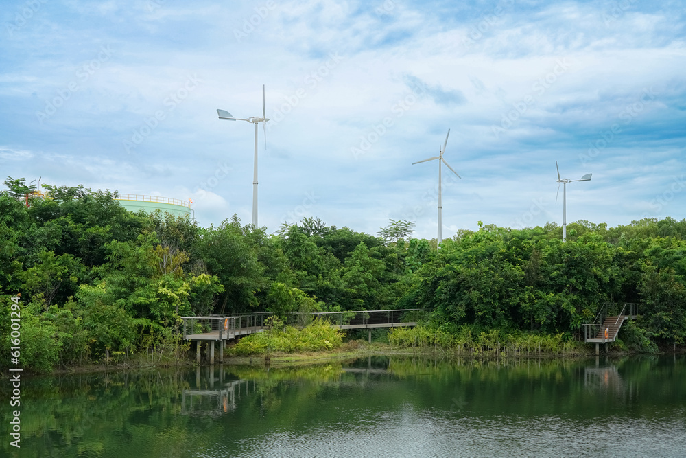 natural environment with tall trees and rivers is home to wind turbines that produce electricity for industrial usage.