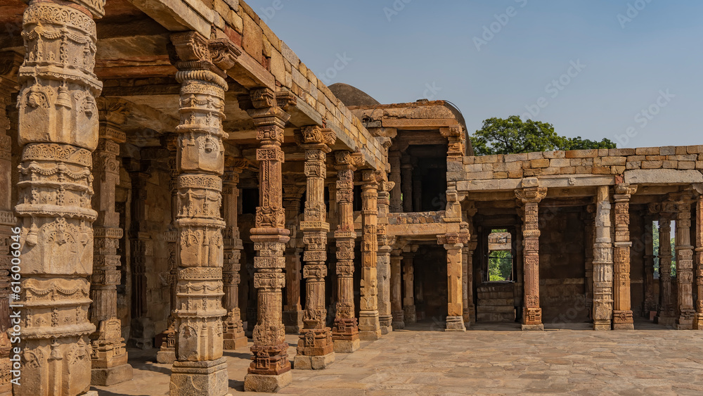 Ruins of the ancient temple complex Qutub Minar. Quwwat-ul-Islam mosque. Gallery with carved columns of red sandstone. Blue sky. Delhi. India. Ruins of the ancient temple complex Qutub Minar. Quwwat-ul-Islam mosque. Gallery with carved columns of red sandstone. Blue sky. Delhi. India.