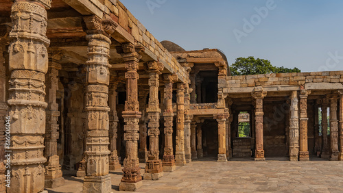 Ruins of the ancient temple complex Qutub Minar. Quwwat-ul-Islam mosque. Gallery with carved columns of red sandstone. Blue sky. Delhi. India.