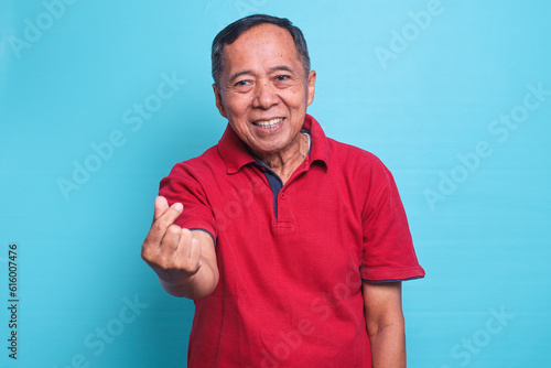 Happy smiling senior Asian man showing heart hand sign or finger heart isolated on blue background