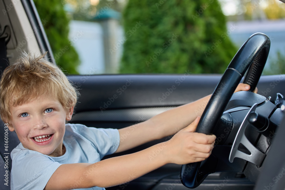 Cute little boy behind the wheel of an expensive car holds the steering wheel, happily looks into the camera. Fulfilling a child's dream of sitting behind the wheel in a real car Cute little boy behind the wheel of an expensive car holds the steering wheel, happily looks into the camera. Fulfilling a child's dream of sitting behind the wheel in a real car