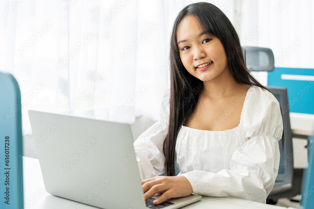 Portrait of a beautiful, young asian woman student smiling as she works on her laptop pc doing research project in a university classroom Portrait of a beautiful, young asian woman student smiling as she works on her laptop pc doing research project in a university classroom