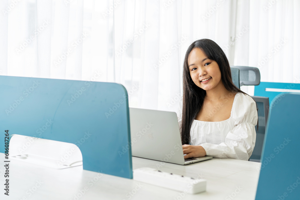 Portrait of a beautiful, young asian woman student smiling as she works on her laptop pc doing research project in a university classroom Portrait of a beautiful, young asian woman student smiling as she works on her laptop pc doing research project in a university classroom