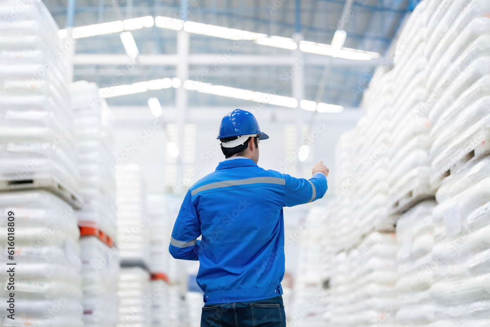 back photo of American male engineers in a large warehouse pointing to the product Wearing a helmet, uniform, surrounded by goods lined up in large plastic and steel material manufacturing plants back photo of American male engineers in a large warehouse pointing to the product Wearing a helmet, uniform, surrounded by goods lined up in large plastic and steel material manufacturing plants