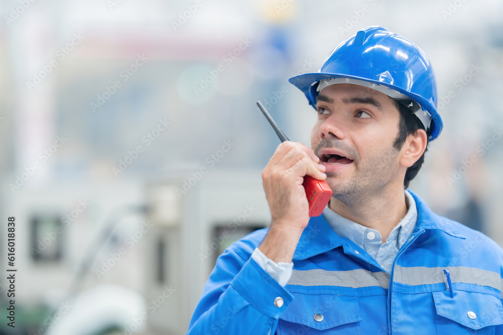 Close-up photo of American male engineer Working diligently and determinedly communicating by radio with employees Wearing uniforms, helmets, Machines working in a large plastic and steel industry Close-up photo of American male engineer Working diligently and determinedly communicating by radio with employees Wearing uniforms, helmets, Machines working in a large plastic and steel industry