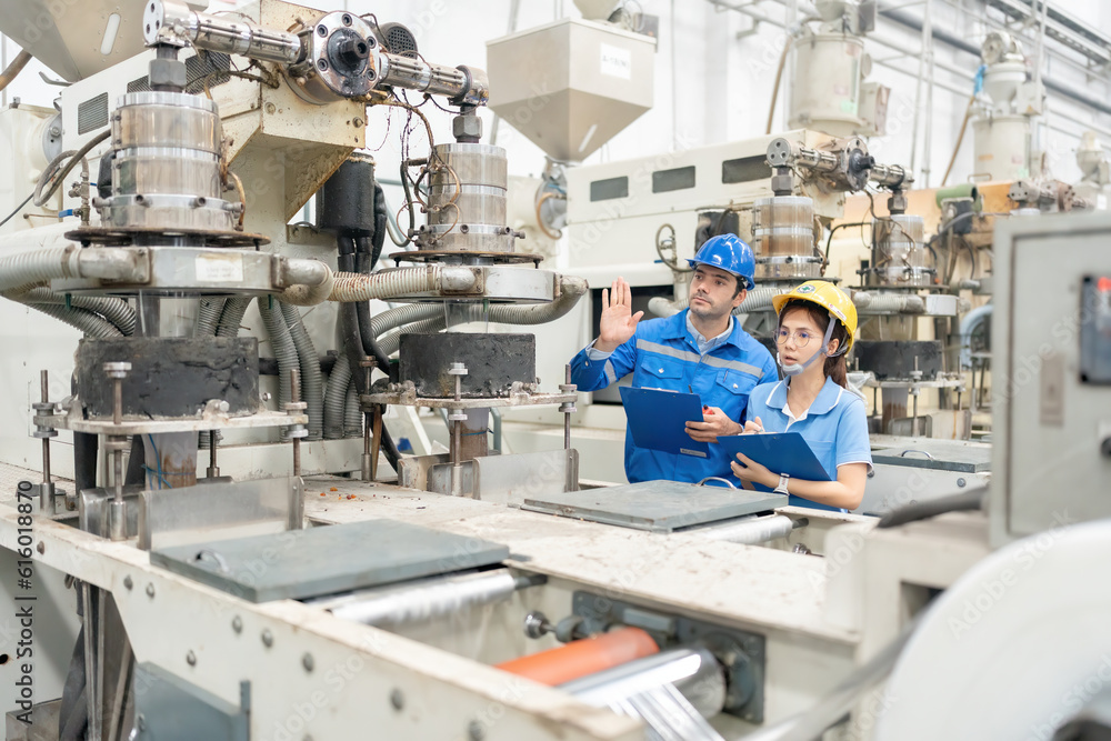 American male engineer manager and female employee wearing helmet, uniform and listnote working and planning business project. in large plastic and steel factories There is a working machine American male engineer manager and female employee wearing helmet, uniform and listnote working and planning business project. in large plastic and steel factories There is a working machine