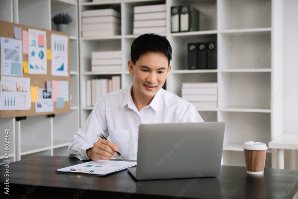 Young Asian business man using laptop and tablet while sitting at her working place. Concentrated at work. Young Asian business man using laptop and tablet while sitting at her working place. Concentrated at work.