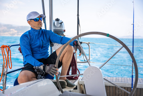 Young man captain stands at the helm and controls a sailboat during a journey by sea