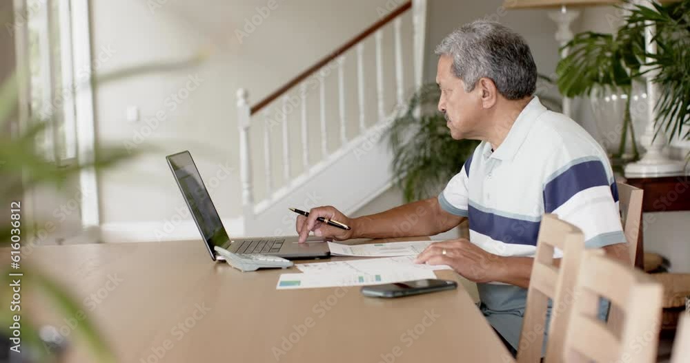 Biracial senior man doing paperwork and using laptop at home, slow motion Biracial senior man doing paperwork and using laptop at home, slow motion