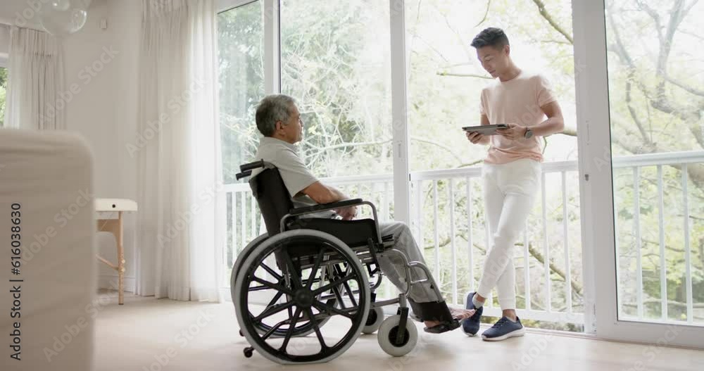 Diverse male physiotherapist with tablet advising and senior man in wheelchair, in slow motion Diverse male physiotherapist with tablet advising and senior man in wheelchair, in slow motion
