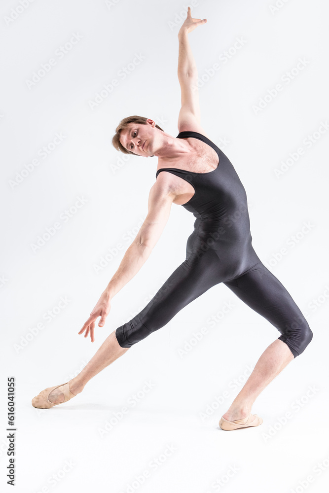 Modern Ballet Dancer Young Caucasian Athletic Man in Black Suit Posing Stretching in Studio On White With Lifted Hands.