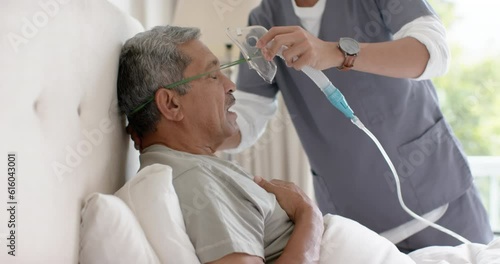 Diverse male doctor helping senior male patient using oxygen mask at home, slow motion photo