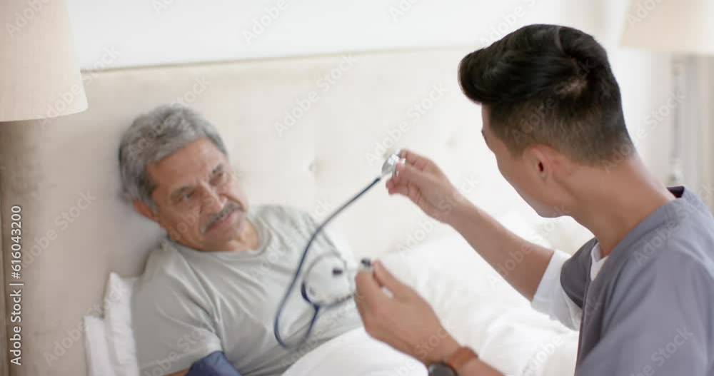 Diverse male doctor testing blood pressure of senior male patient in bed at home, slow motion Diverse male doctor testing blood pressure of senior male patient in bed at home, slow motion