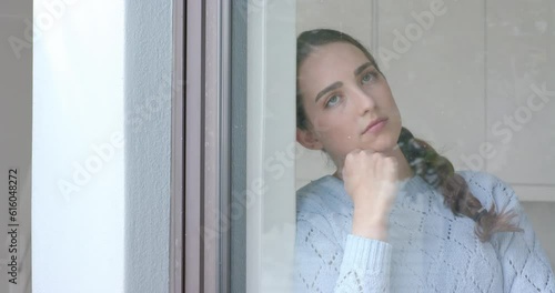 Thoughtful caucasian woman touching her chin at window in slow motion photo