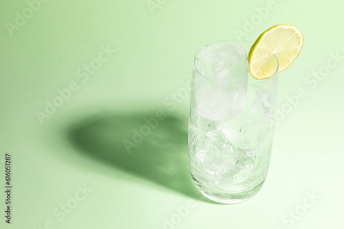 Cold glass full of ice with a lime, ready to serve light green with cast shadow.