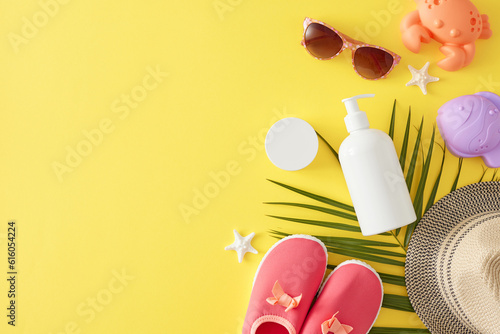 Child-friendly sun protection cream concept. Top view photo of pump bottle, cream jar, beach toys, baby shoes, palm leaf, eyewear, hat, starfish on yellow background with blank space for promo or text