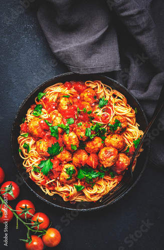 Prepared spaghetti pasta with fried pork meatballs in tomato sauce with parsley in frying pan, black table background, top view