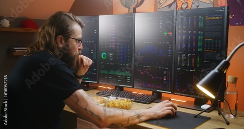 Concentrated trader watches real-time stocks, exchange market charts on multi-monitor computer workstation, types on keyboard. Man works remotely in investment at home office. Cryptocurrency trading. photo