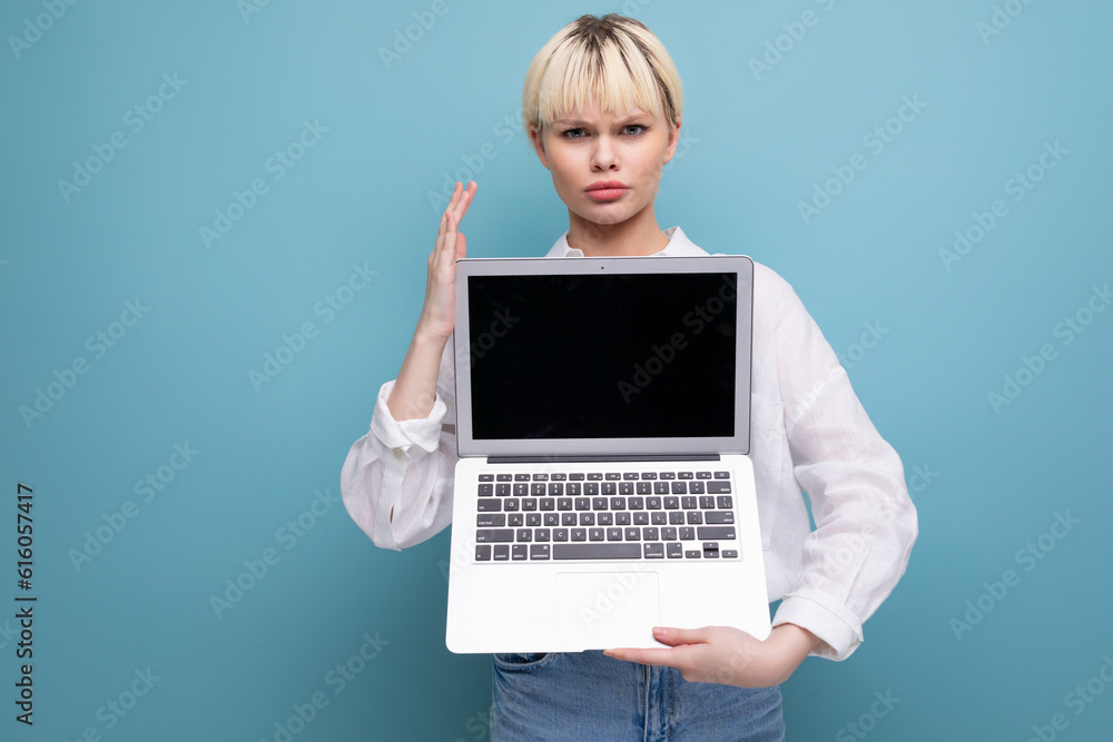 young blond caucasian woman with a short haircut dressed in a white shirt and jeans holds a laptop open with a mockup for advertising young blond caucasian woman with a short haircut dressed in a white shirt and jeans holds a laptop open with a mockup for advertising
